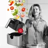 A woman in pajamas is in a kitchen, with an air fryer and vegetables flying out of it. Produktbild-Vorschau