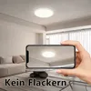 A hand holding a smartphone showing a ceiling light, with the actual ceiling light visible in the background. Náhľad obrázku produktu