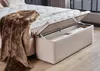 A bedroom scene with a boxspring bed and an open storage ottoman. Produktbild-Vorschau