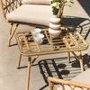 A close-up shot of a rattan coffee table with two white cups and a vase of flowers, placed on a concrete patio with shadows cast by sunlight. Náhled obrázku produktu