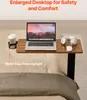 A laptop table is set up on a bed, with a laptop, headphones, a mouse, and a cup holder with a cup on it. Produktbild-Vorschau