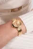 A close-up shot of a woman's wrist wearing a gold Guess watch. Náhled obrázku produktu