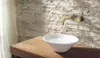 A bathroom sink with a gold faucet mounted on a stone-tiled wall. Podgląd zdjęcia produktu