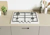 A white gas stovetop is installed on a light wood countertop, with kitchen cabinets below. There are some kitchen accessories and a plant in the background. Voir les images du produit