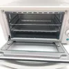 An open white toaster oven with two racks and a baking tray inside. Produktbild-Vorschau