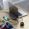 A laptop, tablet, and smartphone are connected to a charging hub on a wooden table, with a cup of coffee and glasses nearby. Anteprima dell’immagine prodotto
