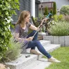 A woman is sitting on stone steps in a garden, holding a gardening tool. Náhľad obrázku produktu