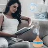 A woman is reading a book while a humidifier releases mist. Anteprima dell’immagine prodotto