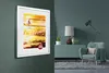 A framed poster is displayed on a wall in a living room setting. Produktbild-Vorschau