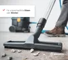 A person is using a vacuum cleaner with a wide brush attachment on a floor with debris. A text box with a checkmark and German text is in the upper left corner. Produktbild-Vorschau