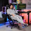 A man is sitting in a gaming chair in a room with colorful lighting and a computer setup. Produktbild-Vorschau