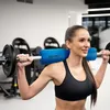 A woman is using a barbell with a blue pad for weight training in a gym. Náhled obrázku produktu