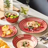 A table setting with plates, bowls, and a glass of water, featuring food items like salad, chicken, and dessert. Náhled obrázku produktu