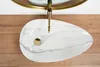 A top-down view of a white oval sink with marble-like veining and a gold faucet. Náhled obrázku produktu