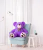 A large purple teddy bear sits in a light blue armchair in a room with white curtains and a floor lamp. Náhľad obrázku produktu