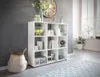 A modern white cube bookshelf filled with decorative items and books, placed in a living room setting with a large window and a rug. Produktbild-Vorschau