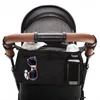 A black stroller organizer attached to the handle of a stroller. Náhled obrázku produktu