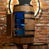 A wooden barrel-shaped wine cabinet with a door open, revealing bottles and a bottle of Jack Daniels, illuminated by blue LED lights, set against a brick wall. Produktbild-Vorschau