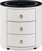 A white, cylindrical nightstand with three drawers and gold ring pulls. The top is black with a circular design and symbols indicating wireless charging. Voir les images du produit