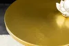A close-up view of a round, brushed gold metal table surface with a decorative white and gold lotus-shaped object on the right side. Produktbild-Vorschau