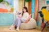 A young girl sits on a beanbag chair holding a plush toy, with a beach-themed backdrop. Náhľad obrázku produktu
