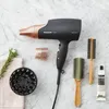 A black Panasonic hair dryer with rose gold accents is displayed on a marble surface, along with hair brushes, a diffuser, and a small tube of product. Podgląd zdjęcia produktu