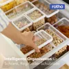 A hand is shown reaching into a drawer filled with clear plastic food storage containers holding various dry goods like cereal and nuts. The containers are neatly organized within the drawer. Produktbild-Vorschau