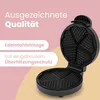 A black heart-shaped waffle maker is open, showing its cooking plates. Text overlays highlight product features. Náhľad obrázku produktu