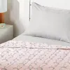 A close-up view of a child's bed with a pink blanket featuring a unicorn and rainbow pattern, and a light gray pillow. Voir les images du produit