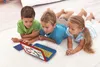 Three children are lying on a white rug, looking at a toy laptop. Anteprima dell’immagine prodotto