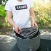 A person is assembling a portable grill outdoors. Produktbild-Vorschau