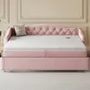 A pink upholstered daybed with a pull-out trundle bed is shown in a room with decorative wall molding. A grey pillow rests on the daybed. Produktbild-Vorschau