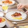 A person is eating a meal from a white plate with a black rim, accompanied by a glass of water with lemon and a side dish in a bowl. Produktbild-Vorschau
