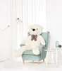 A large white teddy bear sits in a light blue armchair in a brightly lit room with sheer white curtains. Podgląd zdjęcia produktu