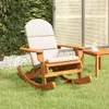 A wooden rocking chair with beige cushions sits on a grassy lawn next to a small wooden table with a cup on it. In the background, there is a hedge and a decorative screen. Voir les images du produit