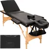 A black massage table with wooden legs is shown against a white background. A folded massage table case is also visible in the lower left corner. Voir les images du produit