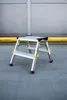 A step stool is placed on a concrete surface in front of a large gray wall with a yellow stripe. Podgląd zdjęcia produktu