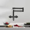 A black wall-mounted kitchen faucet is shown against a white wall, with a countertop and sink area visible below. Podgląd zdjęcia produktu