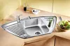 A stainless steel corner sink with a faucet, drainboard, and a small compartment holding green onions, set on a light brown countertop. A bowl of salad is visible to the right. Náhľad obrázku produktu