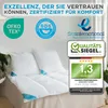 A close-up of white pillows and a comforter on a bed, with various certification logos and a review rating displayed prominently. Produktbild-Vorschau