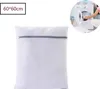 A white laundry bag with a gray zipper is shown in the foreground, with a small inset image of a person putting laundry into a washing machine in the background. Produktbild-Vorschau