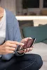 A person is using a smartphone indoors, with a couch and pillows in the background. Produktbild-Vorschau
