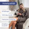 A woman is sitting in a chair reading a book while wearing a bathrobe. Produktbild-Vorschau