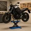 A black motorcycle is elevated on a blue scissor lift in a garage setting with tools on the wall. Náhľad obrázku produktu