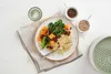 A plate of food with couscous, broccoli, and pumpkin, served with a small dish of sauce and a bowl of sesame seeds. Anteprima dell’immagine prodotto