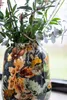 A close-up shot of a decorative vase filled with greenery, placed near a window. Produktbild-Vorschau