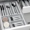 A close-up view of a cutlery organizer in a kitchen drawer, filled with various utensils and small containers. Produktbild-Vorschau