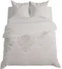 A top-down view of a beige bedding set with ornate patterns, including two pillows and a duvet cover, laid out on a white surface. Podgląd zdjęcia produktu
