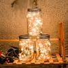 Three mason jar lanterns with LED string lights are displayed on a wooden shelf, with some greenery and berries in the foreground. Produktbild-Vorschau