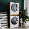 A laundry room scene with a stacked washer and dryer unit, a storage cart, and plants. Náhled obrázku produktu